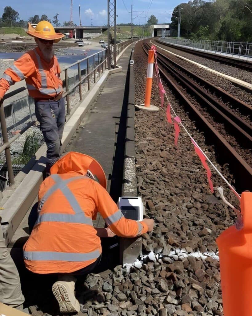 Technicians installing a monitoring device on the rail track as part of the Coomera railtrack monitoring system.
